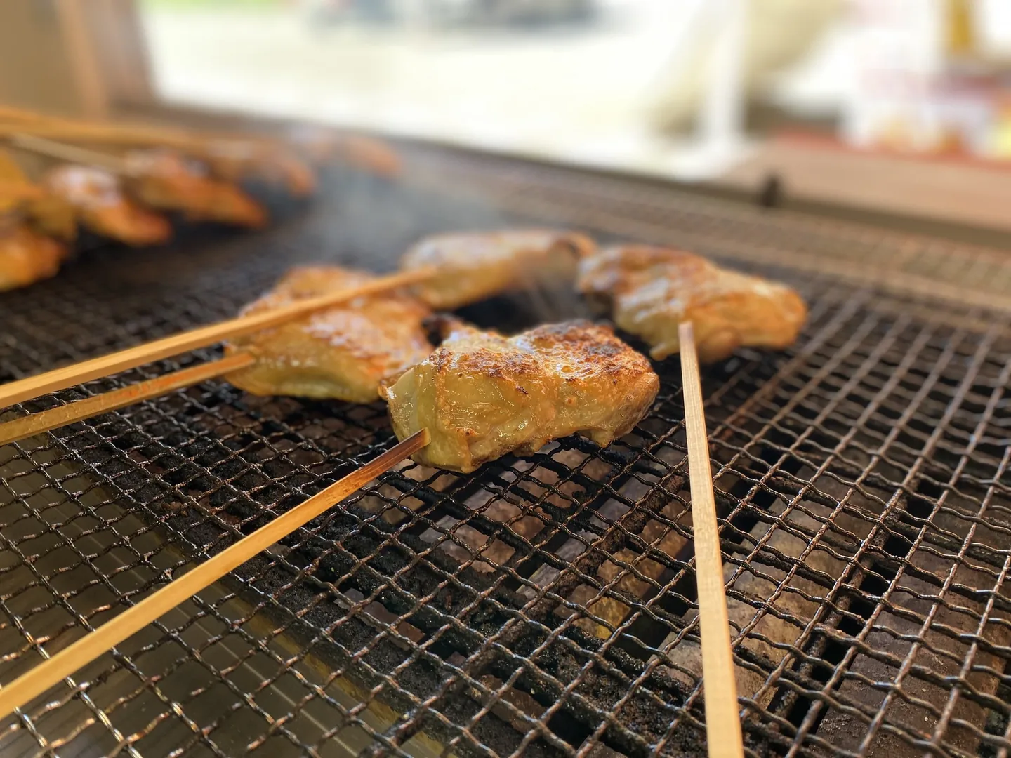 網の上で焼かれる串に刺した鶏肉